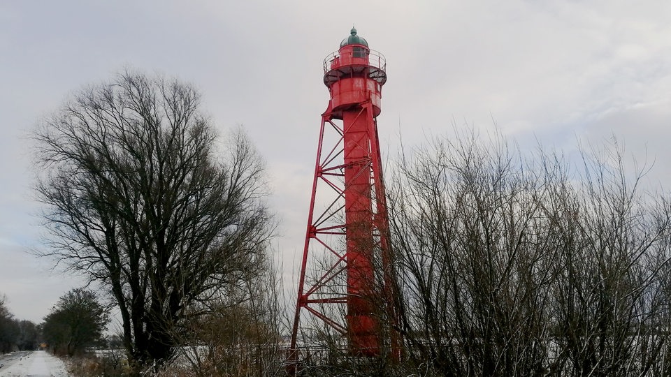 Ein alter roter Leuchturm steht in einer verschneiten Landschaft.