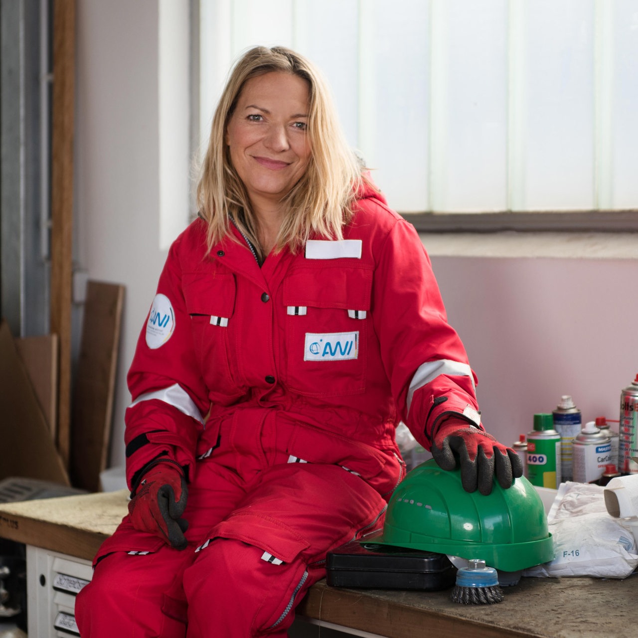 Antje Boetius sitzt in einem roten Overall auf einer Werkbank