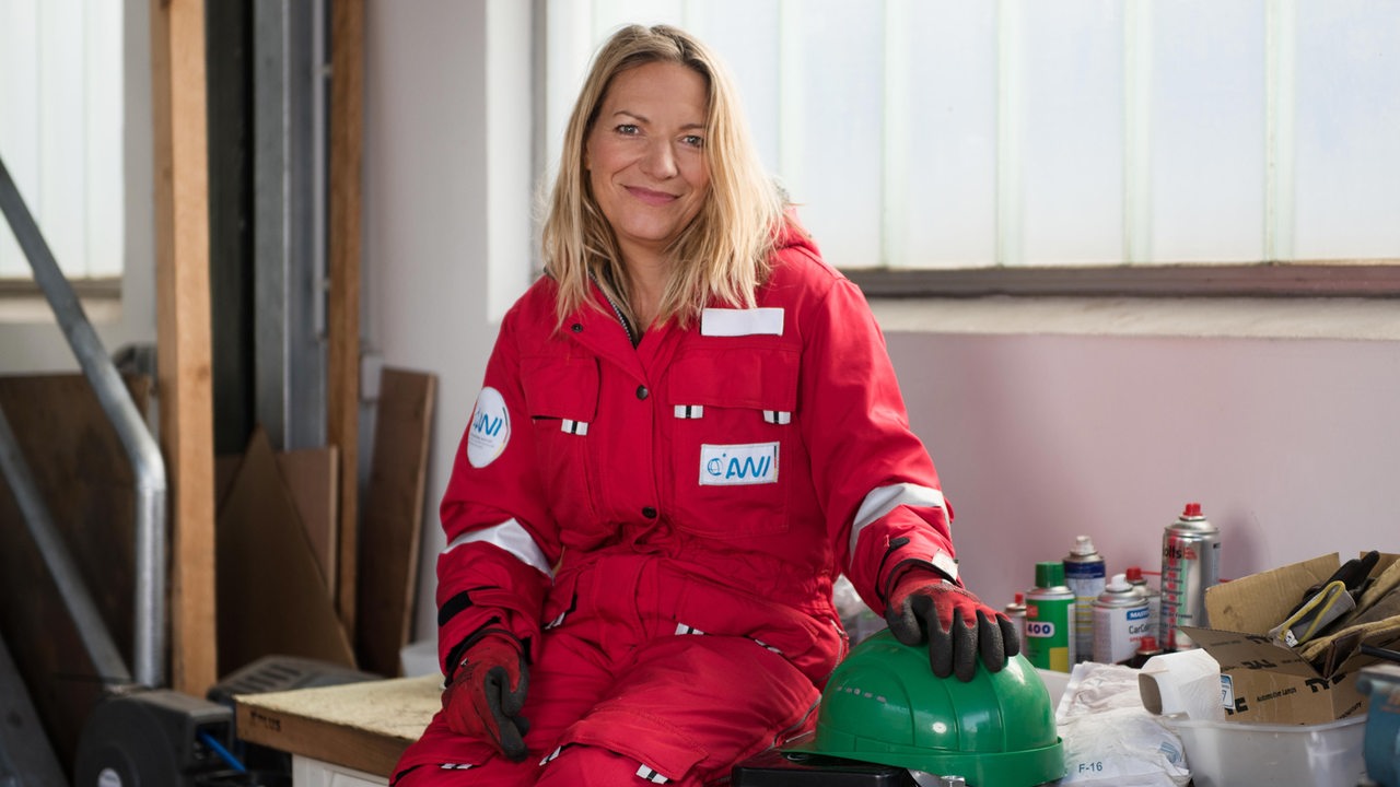 Antje Boetius sitzt in einem roten Overall auf einer Werkbank