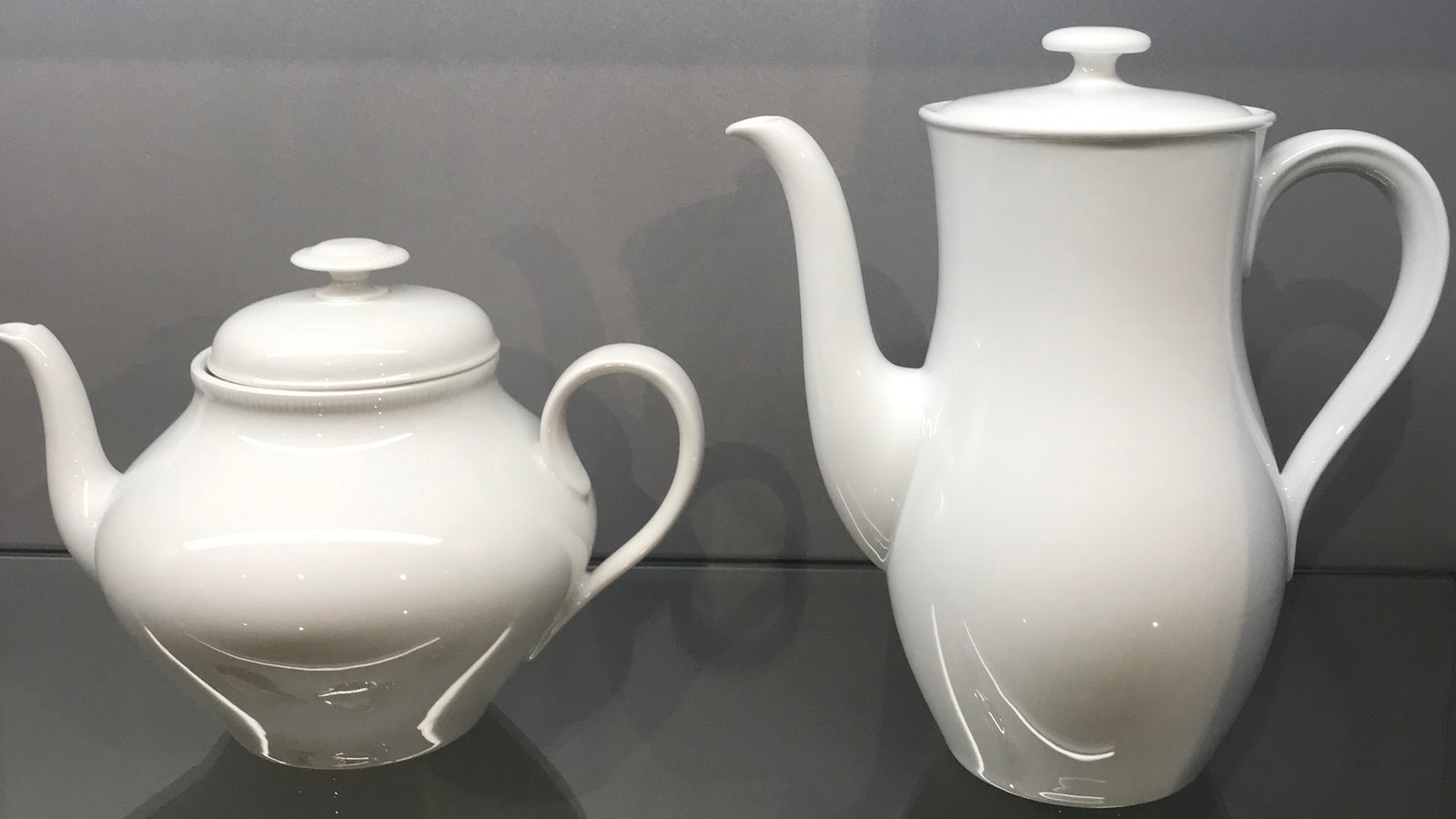 Eine Tee- und eine Kaffeekanne aus weißem Porzellan stehen in einer Ausstellungsvitrine.