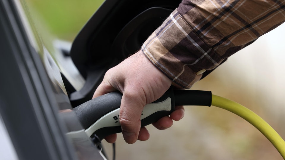Eine Hand hält ein Aufladekabel für ein Auto