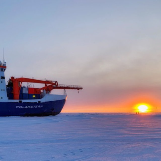 28.8.: Die Polarstern bei tiefstehender Sonne im Eis, vorne ein Besatzungsmitglied mit einem Schlitten