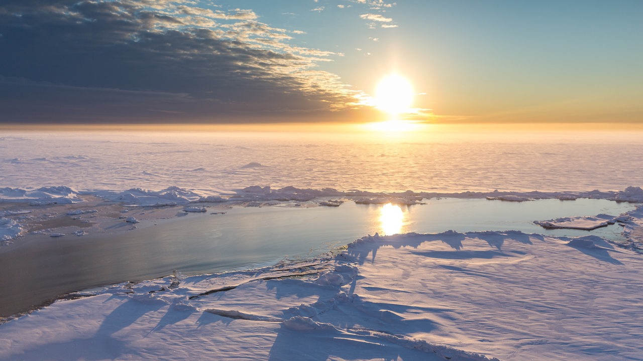 Blick in die Arktis während die tiefhängende Sonne am Horizont zu sehen ist.