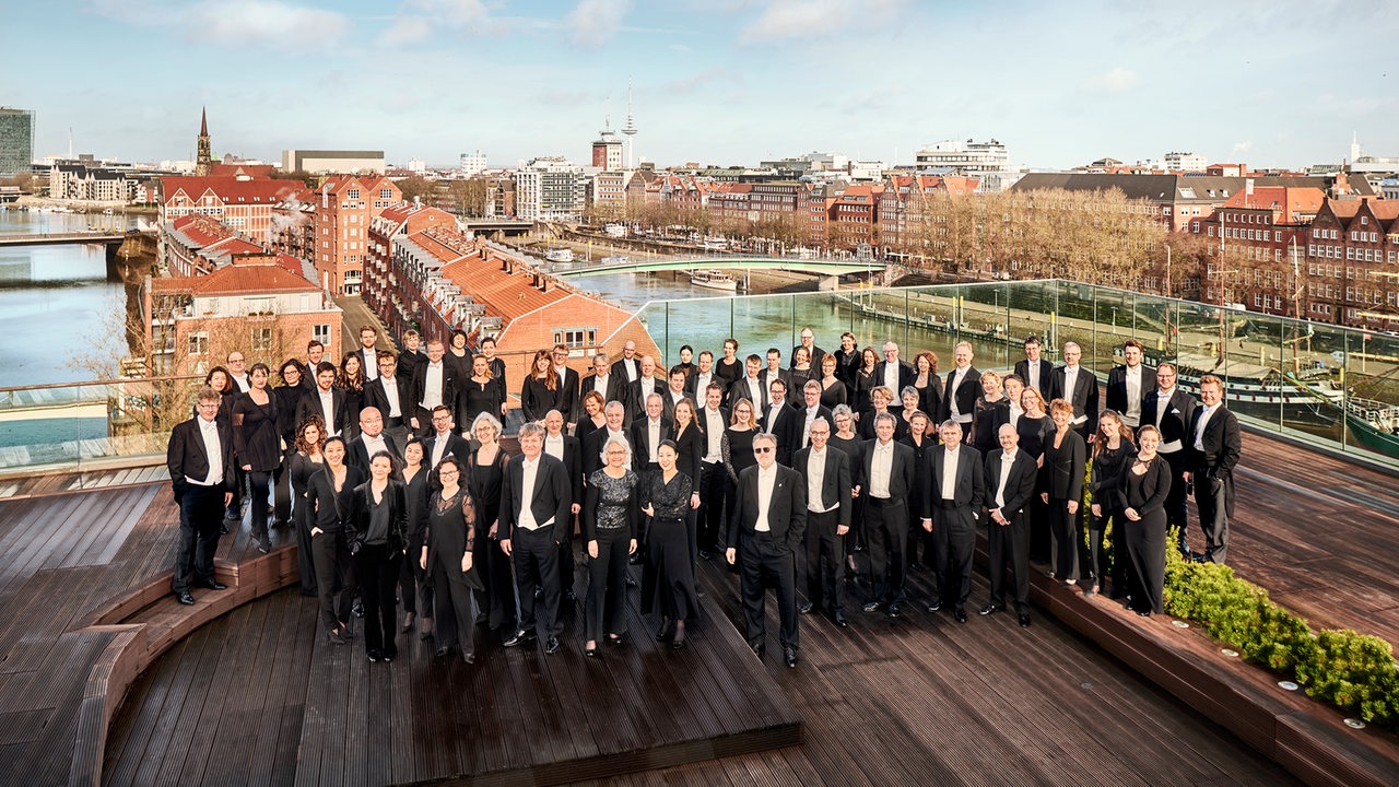 Das Orchester der Bremer Philharmoniker auf einer Dachterasse vor der Skyline der Bremer Innenstadt.