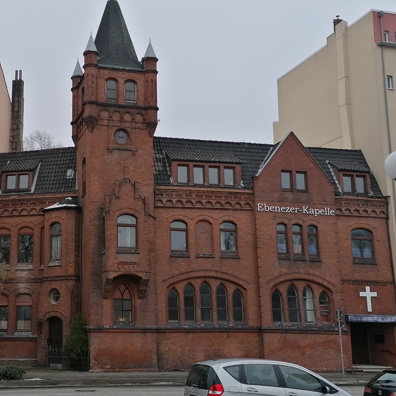 die Klinkerfassade einer Kirche, rechts und links davon Mietshäuser