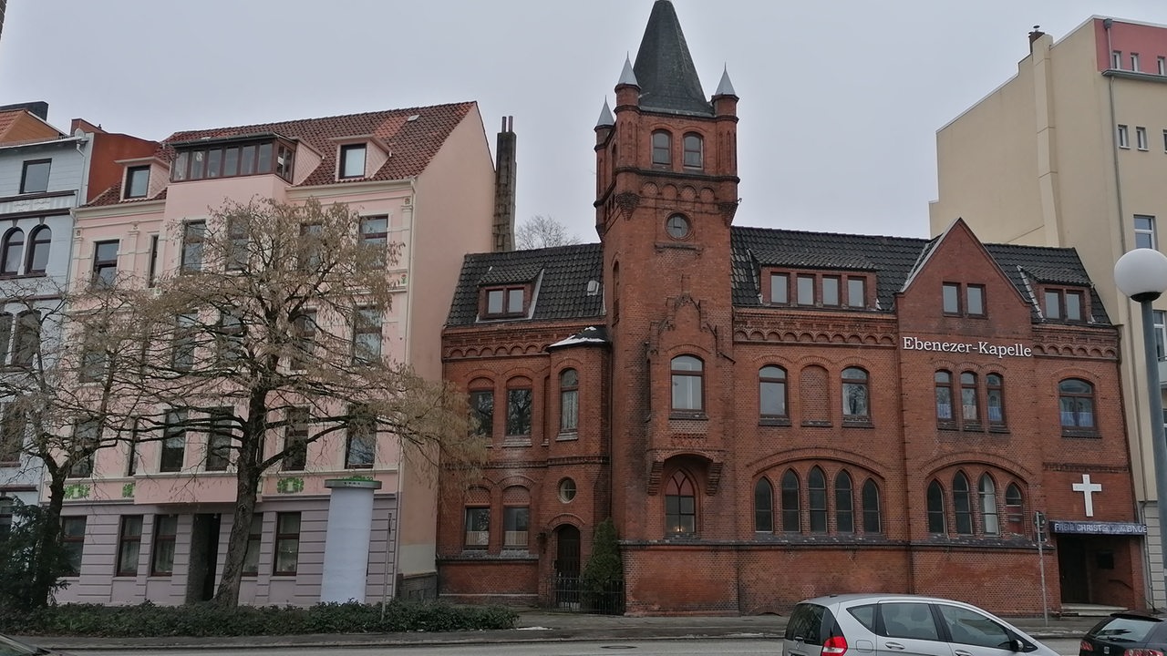 die Klinkerfassade einer Kirche, rechts und links davon Mietshäuser