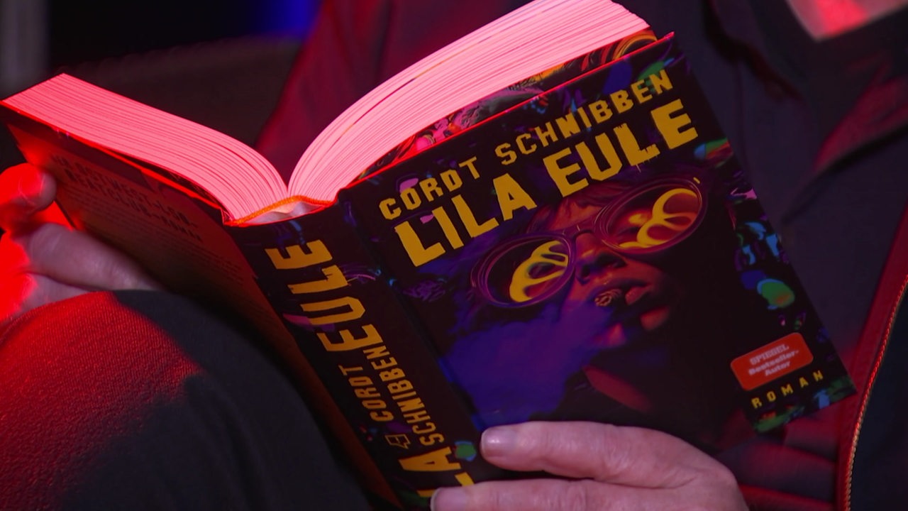 Hände halten das Buch "Lila Eule" von Cordt Schnibben aufgeschlagen