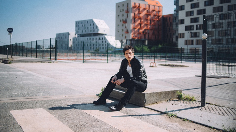 Charles Pasi sitzt auf einem Betonklotz vor Hochhäusern.
