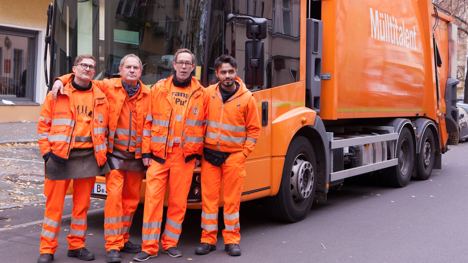 Eine Gruppe von Müllmännern steht vor einem orangefarbenen Müllauto.