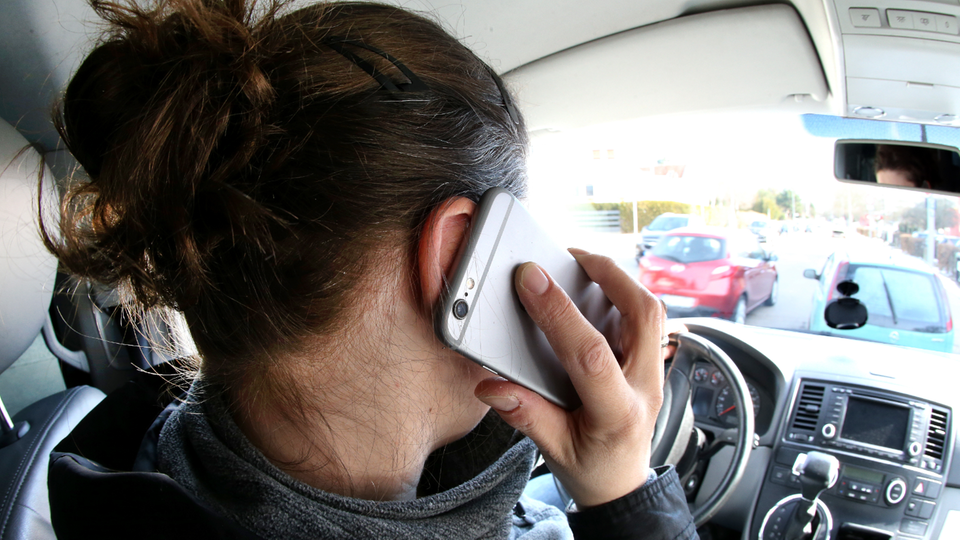 Eine Frau hält ein Mobiltelefon an ihr Ohr, während sie Auto fährt.