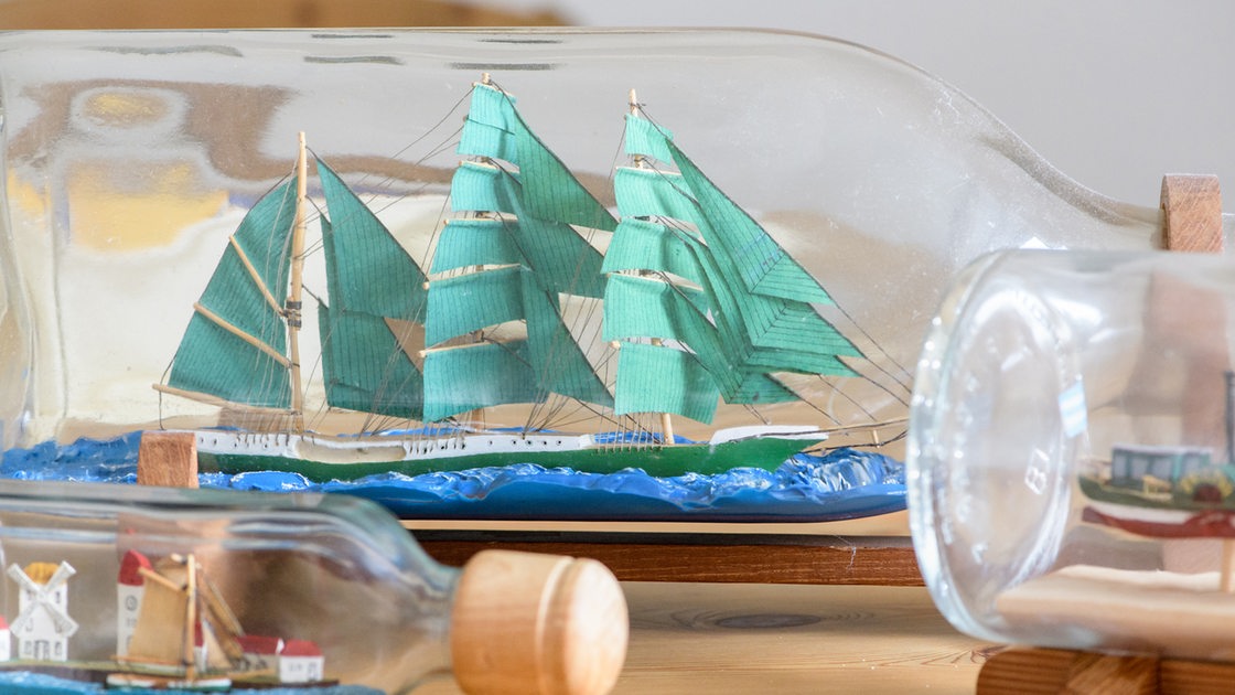 Eine Flasche mit einem Modell des Segelschiffs "Alexander von Humboldt" steht neben weiteren Buddelschiffen auf einem Tisch