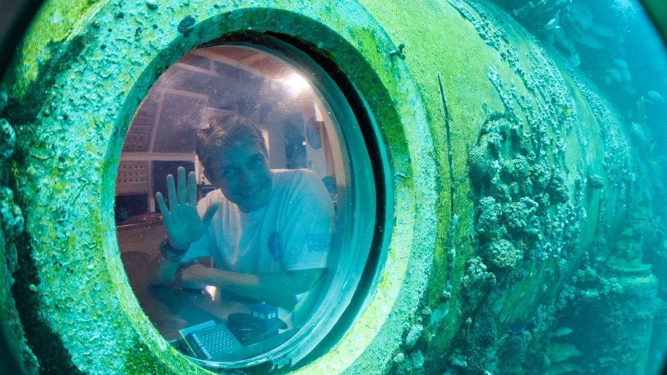 Fabien Cousteau winkt aus dem Bullauge des Unterwasserlabors Aquarius