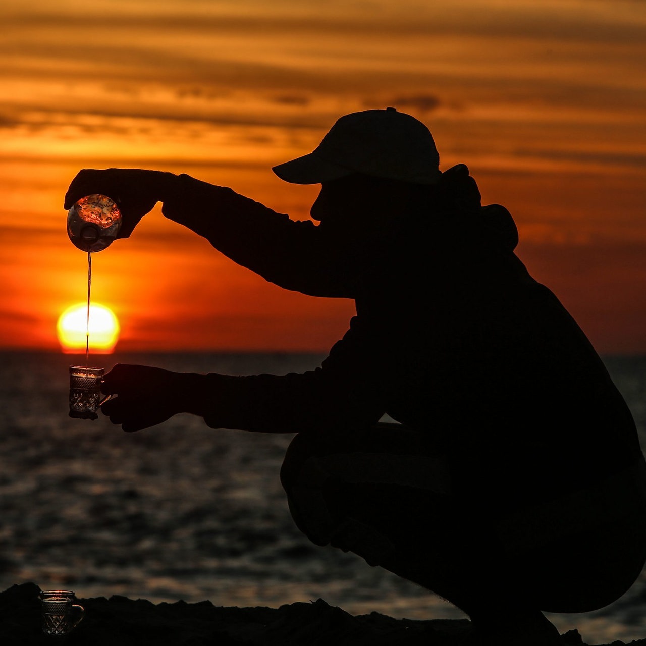 Ein Mann am Hafen von Rafah in Gaza schenkt sich einen Tee ein, während im Hintergrund die Sonne untergeht (Symbolfoto)