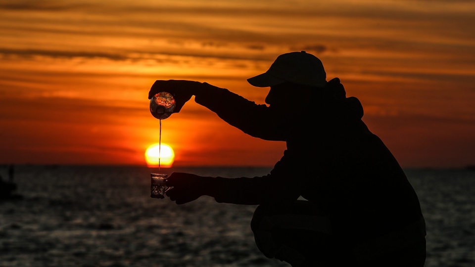 Ein Mann am Hafen von Rafah in Gaza schenkt sich einen Tee ein, während im Hintergrund die Sonne untergeht (Symbolfoto)