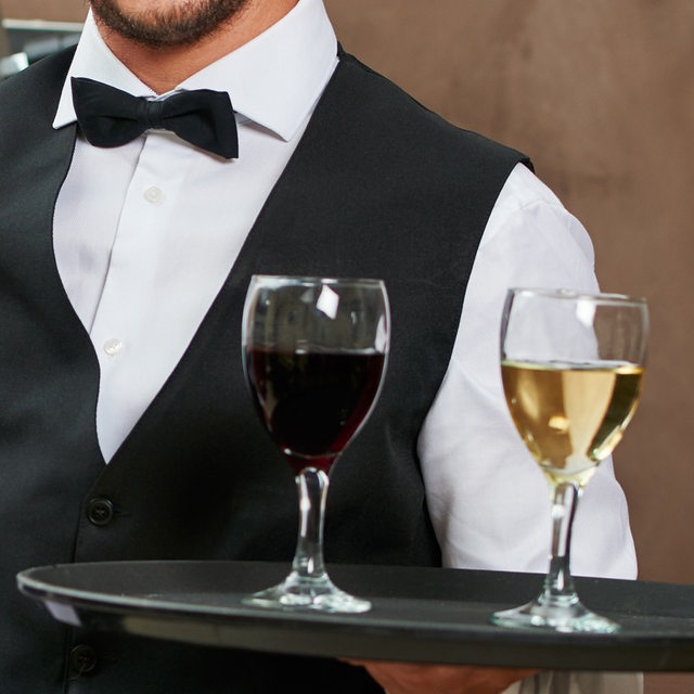 Ein Oberkellner mit einem Tablett, auf dem ein Rot- und ein Weißwein steht (Symbolbild)