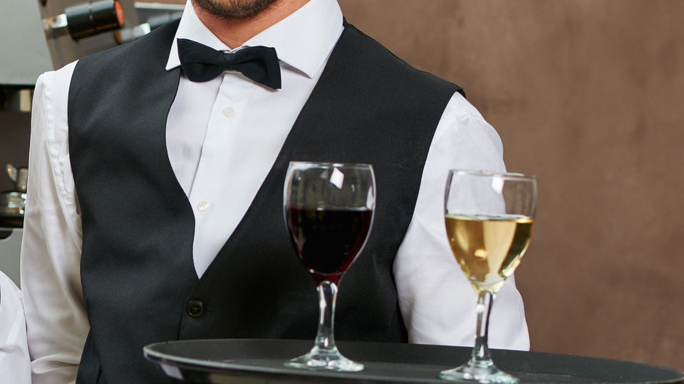 Ein Oberkellner mit einem Tablett, auf dem ein Rot- und ein Weißwein steht (Symbolbild)