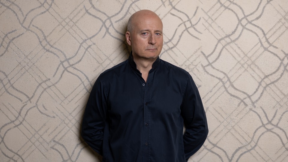 Dirigent Paavo Järvi lehnt an eine Wand und schaut in die Kamera