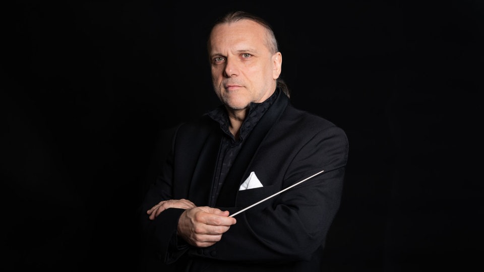 Dirigent Enrique Ugarte steht vor einem schwarzen Hintergrund