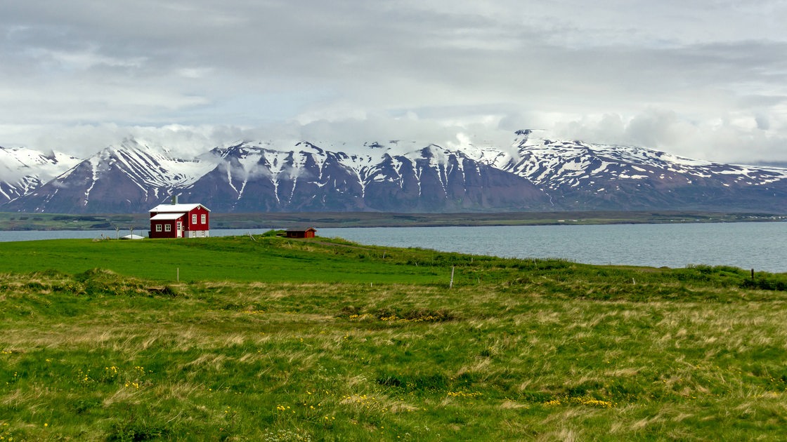 Ein Wohnhaus an einem Fjord in Island mit grünen Feldern und Bergen. (Symbolbild)