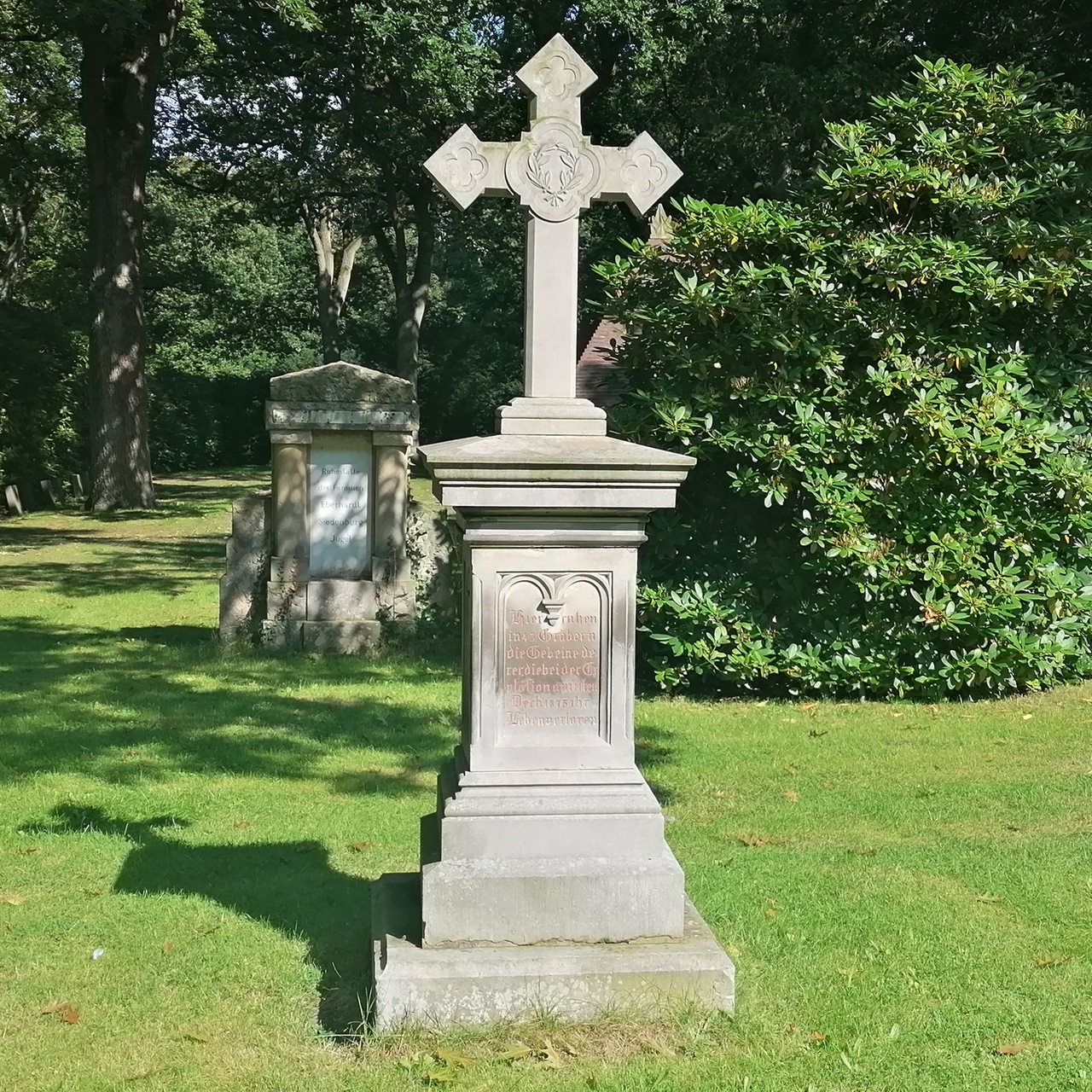 Ein grauer Gedenkstein mit einem großen Kreutz auf einem Friedhof