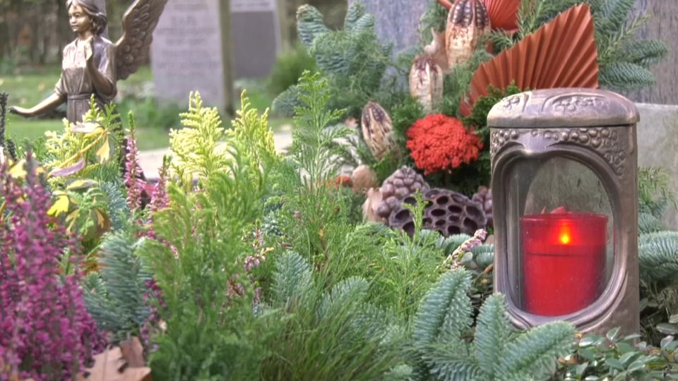 Ein Grablicht mit vielen Blumen auf einem Friedhof.
