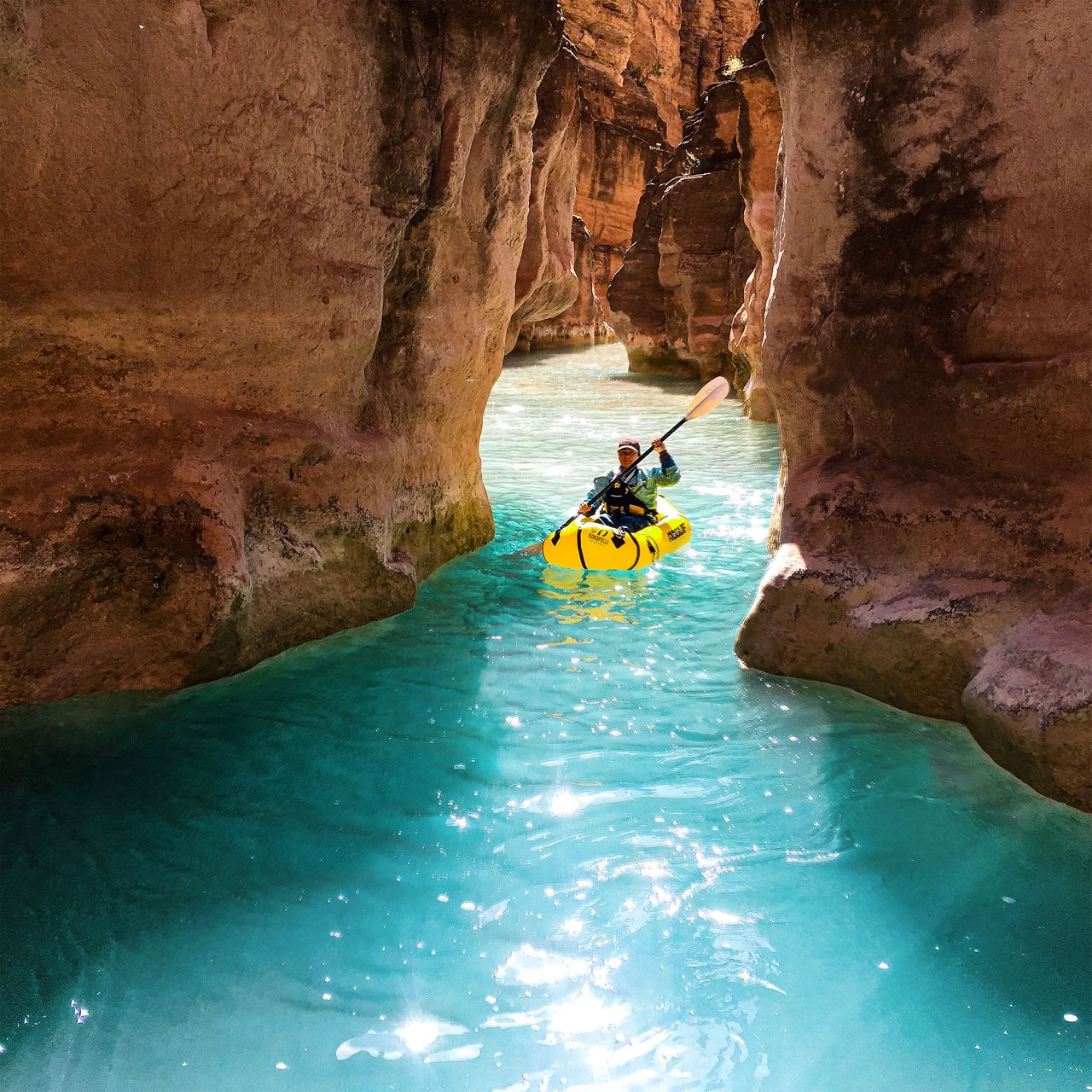 Eine Frau paddelt zwischen rot-gelben Felsformationen des Grand Canyons in blauem Wasser