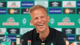 Trainer Markus Anfang strahlend bei seiner offiziellen Vorstellung bei Werder Bremen vor einer Werbewand.
