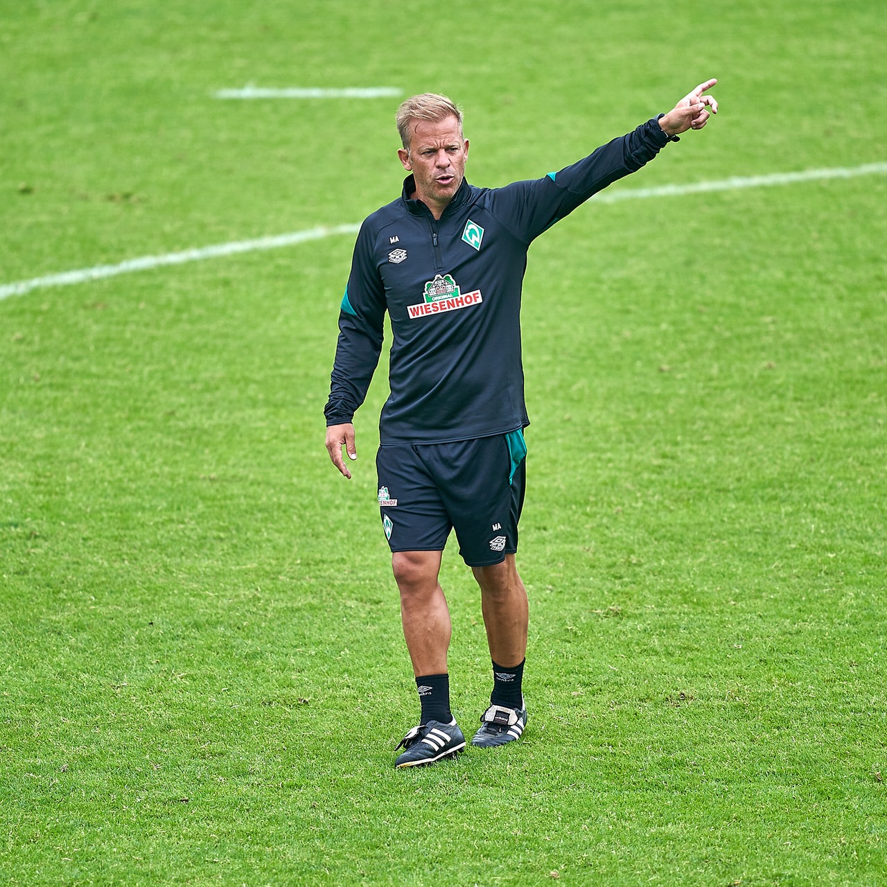 Werder-Training Markus Anfang ruft über den Trainingsplatz und streckt den Arm aus.