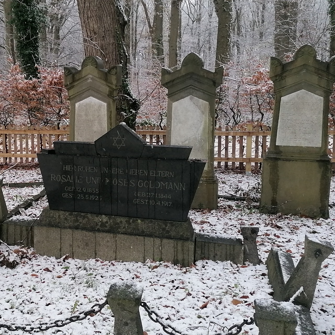 ein schwarzer Marmorgrabstein, dahinter und links Grabsteine aus Sandstein