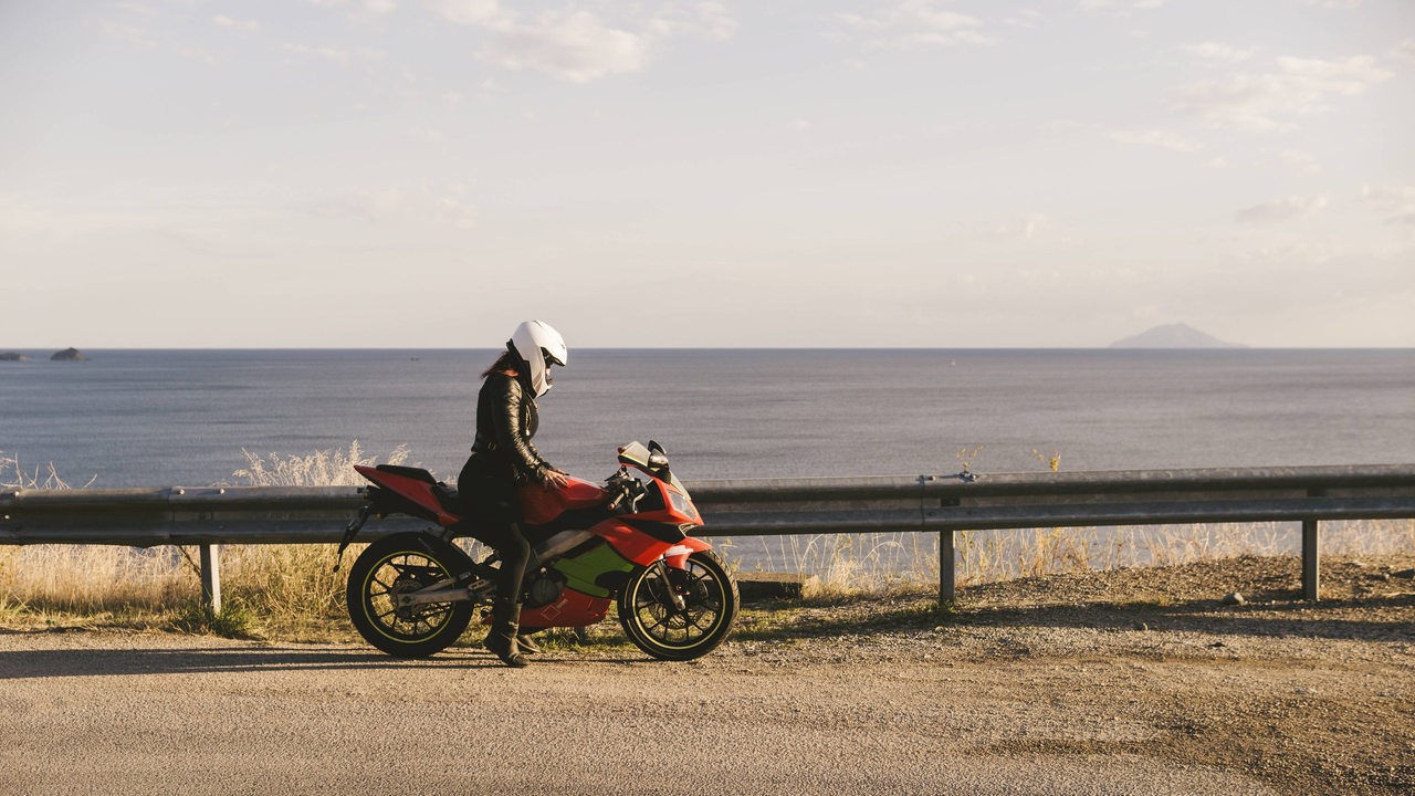 Eine Motoradfahrerin auf ihrem Motorrad an einer Küste.