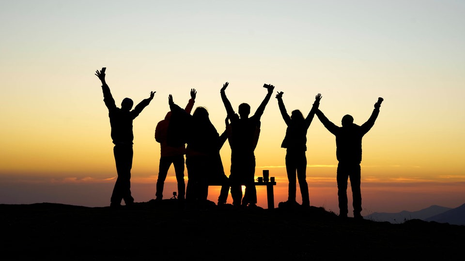 Silhouette feiernder Menschen vor einem Sonnenuntergang
