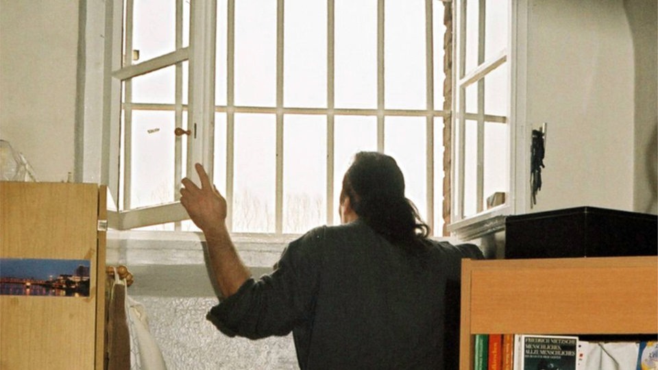 Ein Mann steht in einer Gefängniszelle und schaut aus dem vergitterten Fenster (Symbolbild)