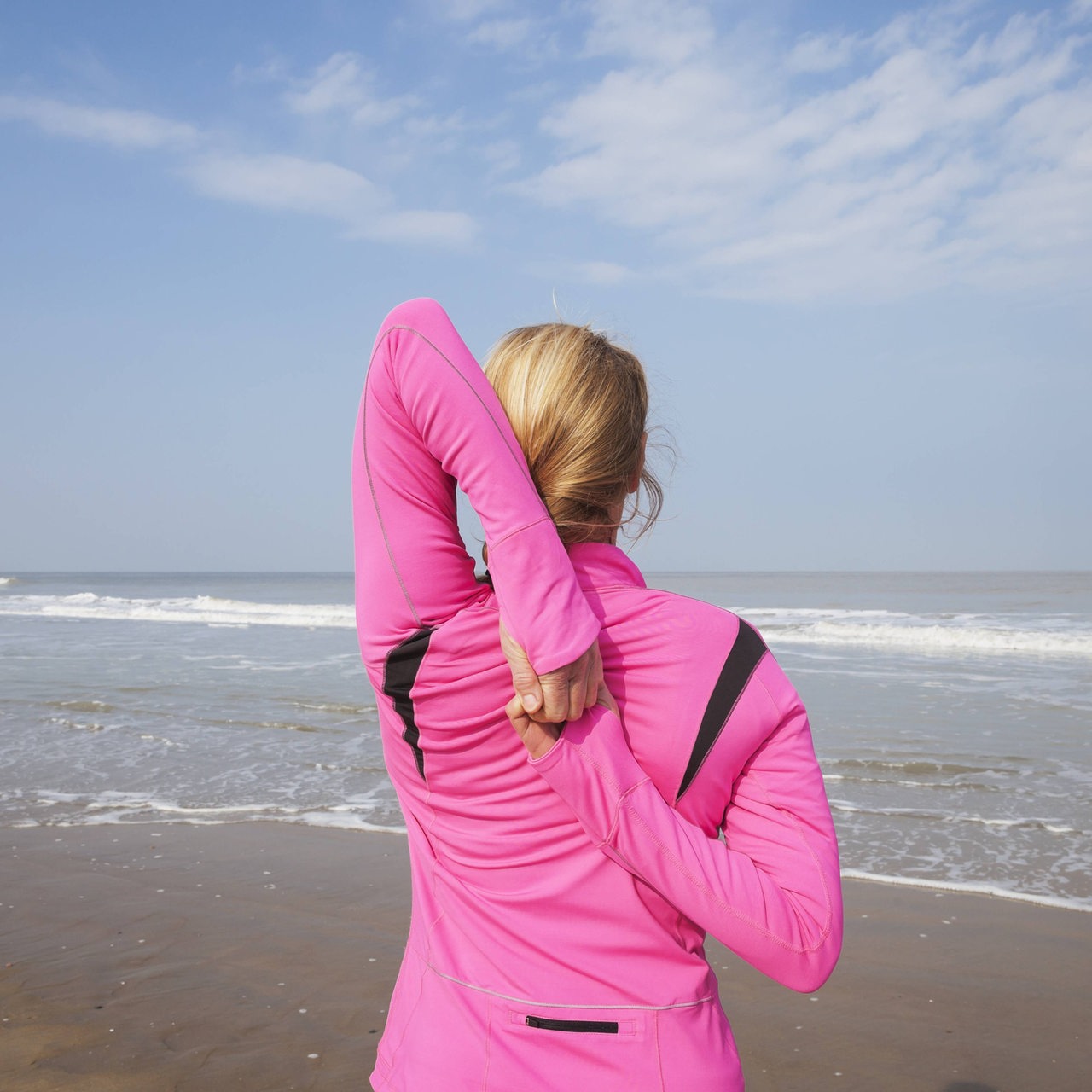 Eine Frau in Sportkleidung dehnt sich an einem Strand (Symbolbild)