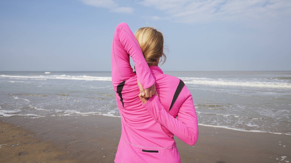 Eine Frau in Sportkleidung dehnt sich an einem Strand (Symbolbild)