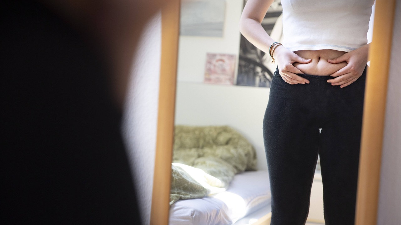 Gewichtskontrolle einer jungen Frau vor dem Spiegel (Symbolbild)