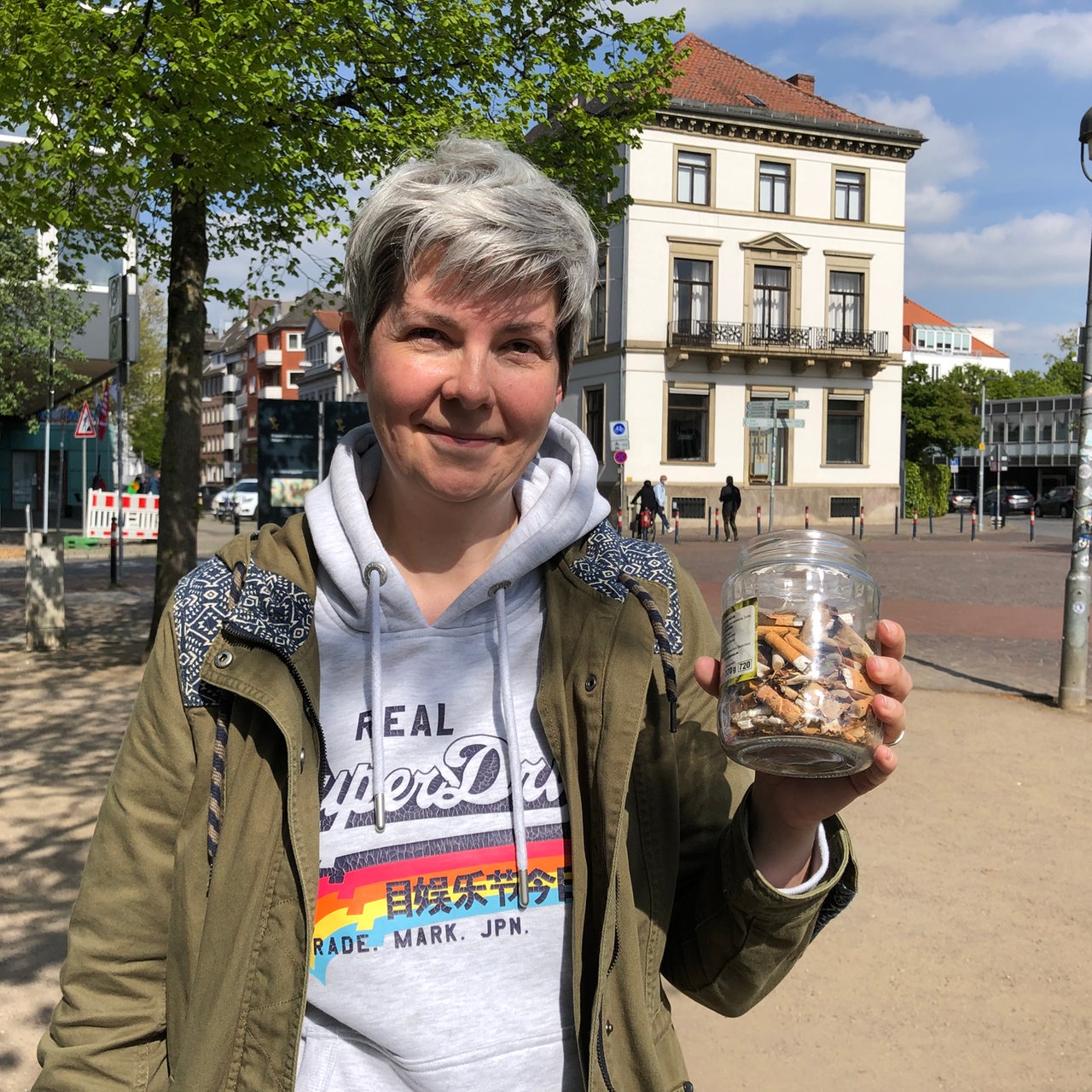 eine Frau hält ein Glas mit Zigarettenkippen