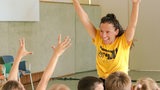 Eine Frau begrüßt mit erhobenene Armen eine Gruppe Kinder.