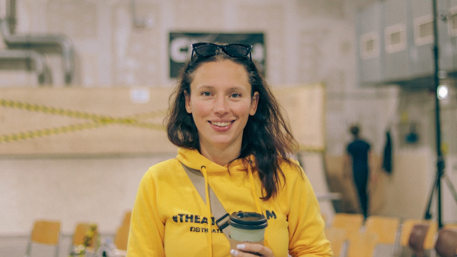 Eine Frau mit einem Kaffeebecher in der Hand lächelt in die Kamera.