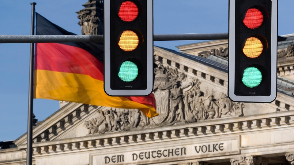 Themenbild Ampelkoalition, zwei Ampeln zeigen alle Fahnen vor dem deutschen Reichstagsgebäude