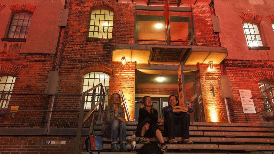 Menschen sitzen bei Dunkelheit auf einer Treppe vor dem Speicher IX