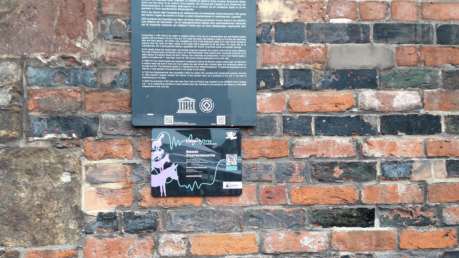 An einer Backsteinwand ist ein Schild mit QR-Code und Bremer Stadtmusikanten der Lauschorte zu sehen