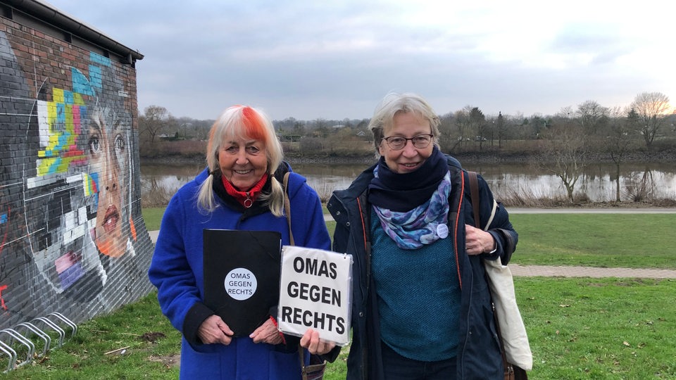 Zwei Frauen stehen an der Weser und halten Papier hoch, auf dem "Omas gegen Rechts" steht