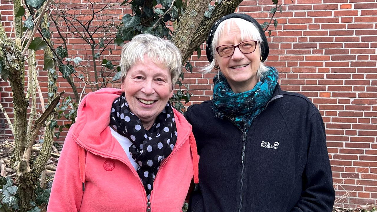 Zwei Frauen stehen nebeneinander und lachen in die Kamera