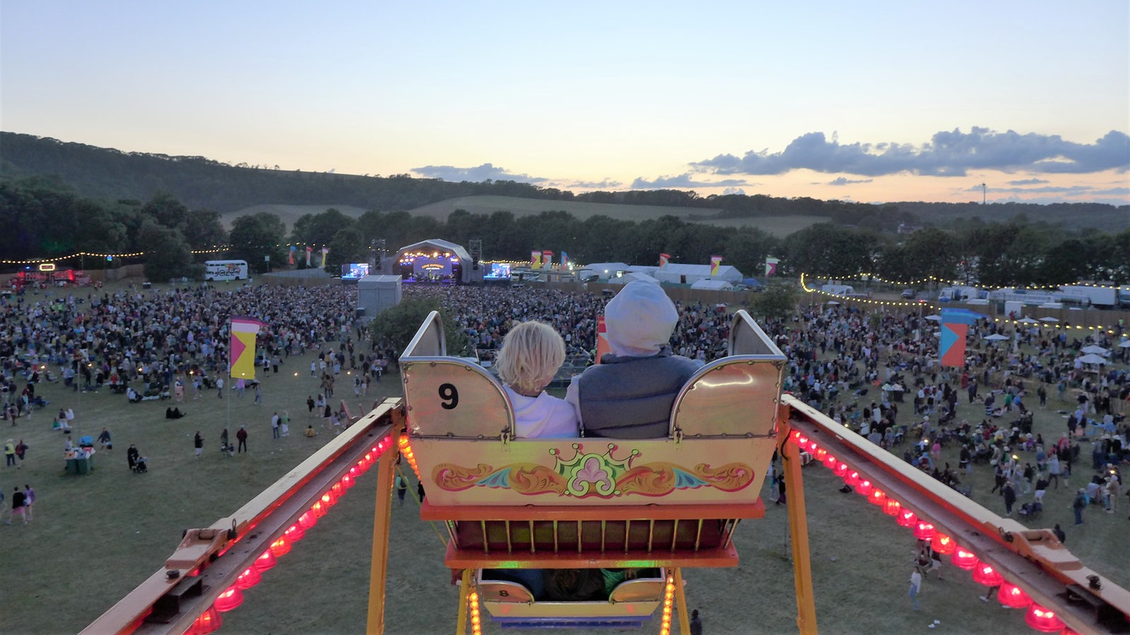 Zwei Zuschauer sitzen in einer Karroussel-Gondel über dem Festivalgelände