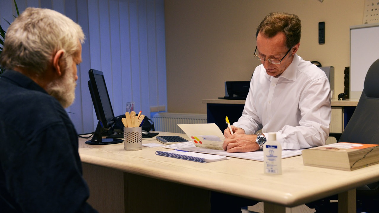 Ein älterer Mann sitzt im Sprechzimmer eines Hausarztes