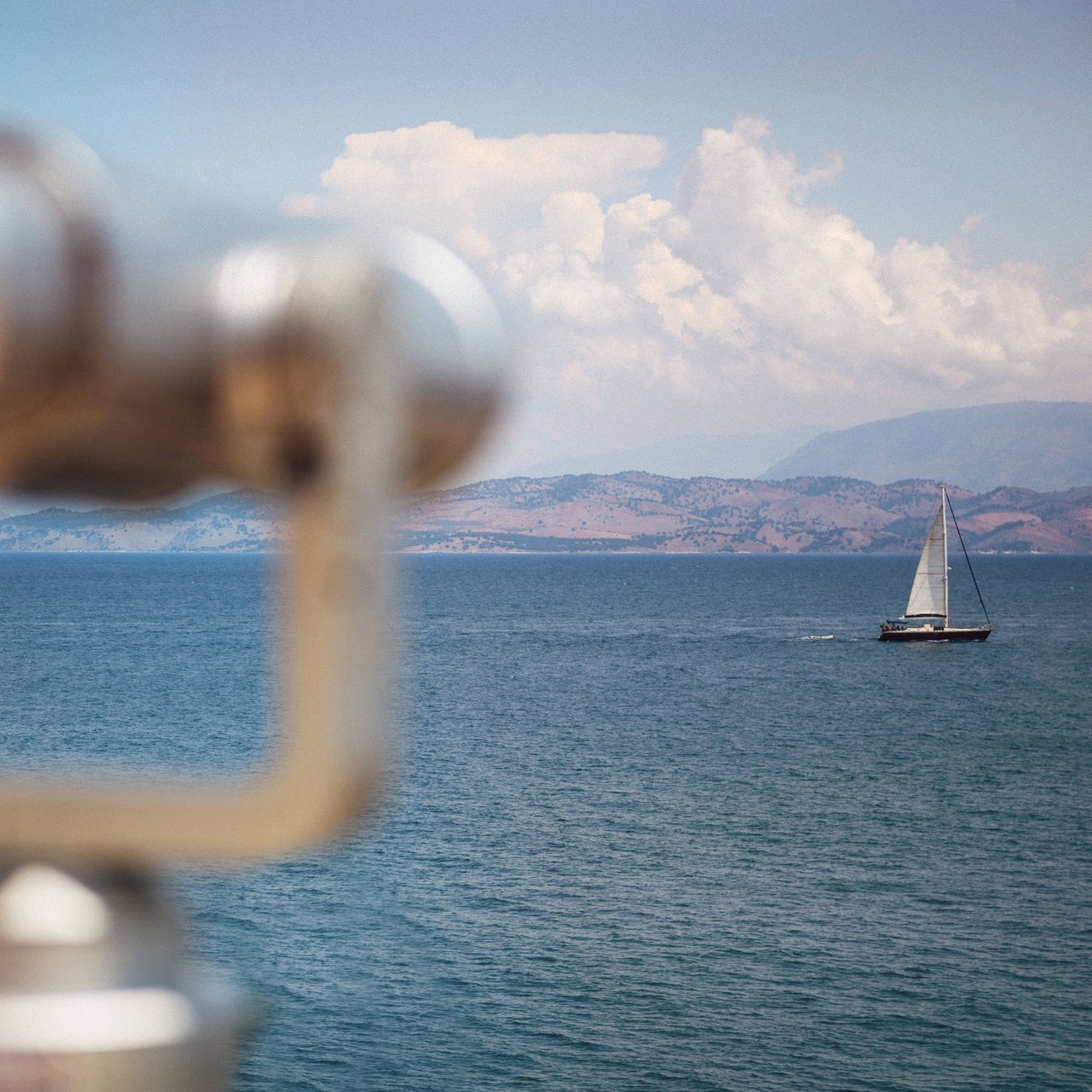 Ein Meer mit Segelboot, im Hintergurnd Küste, im Vordergrund ein unscharfes Fernglas (Symbolbild)