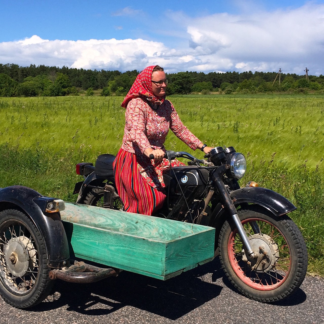 Eine Frau mit rotem Rock fährt auf einem Moped mit Beiwagen.