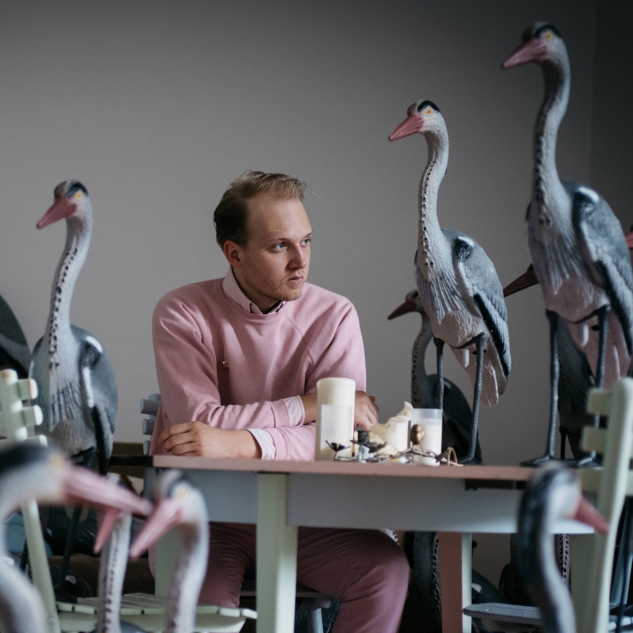 Pressebild: Richard Leßmann sitzt an einem Tisch inmitten von Kranichskulpturen 