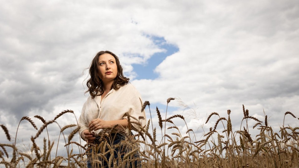 Milena Glimbovski, Autorin von "Über Leben in der Klimakriste", steht auf einem Kornfeld und schaut nachdenklich zum Horiziont in den Himmel.