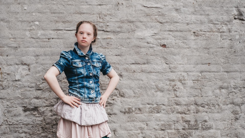 eine junge Frau steht vor einer grauen Mauer